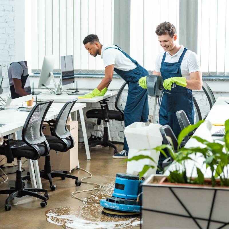 Two workers focusing on cleaning the office and smiling.