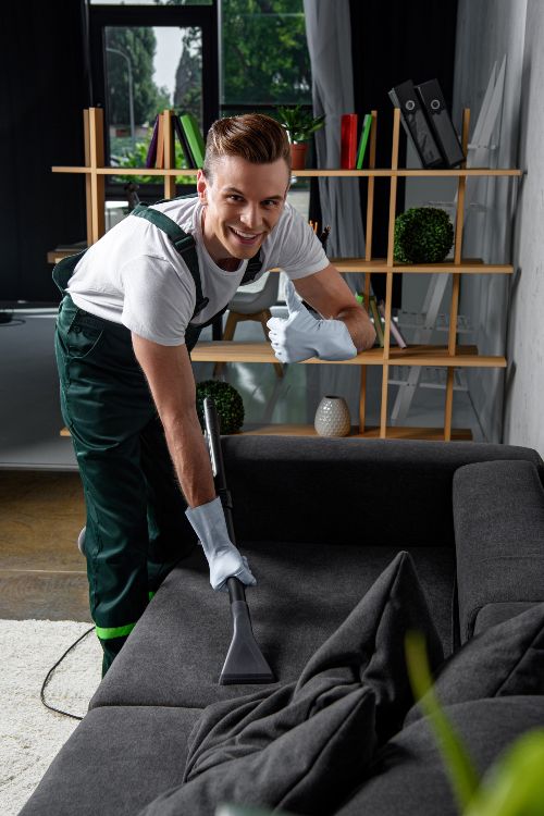 A cleaning guy performing a vacuum cleaning of a sofa.