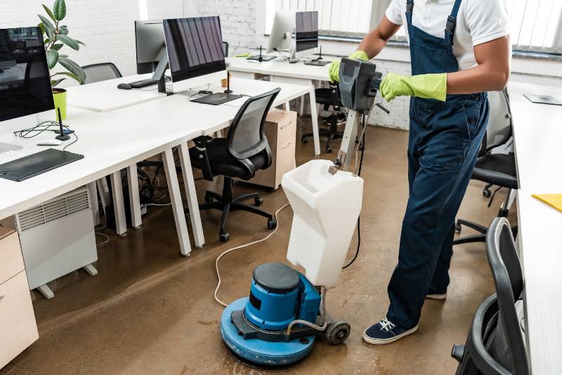 A half body of a worker operating a cleaning device on the floor of the office.